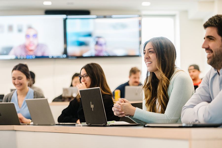 Several students are seated at tables, each with a laptop computer in front of them. 