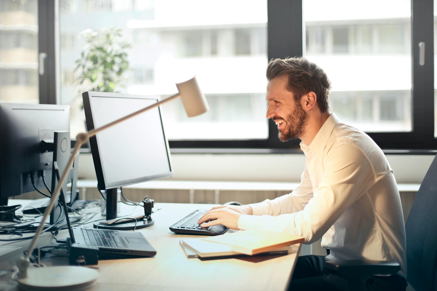 IT professional smiling while working at a computer in a modern office—representing career outcomes of MSIT and MBA degree paths.
