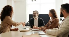 A candidate shaking hands with an interviewer in a professional setting, symbolizing career opportunities with a master’s in human resource management. Three other professionals observe and take notes during the meeting.