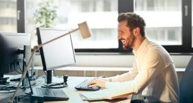 IT professional smiling while working at a computer in a modern office—representing career outcomes of MSIT and MBA degree paths.
